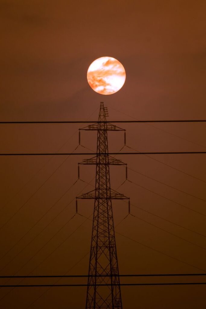 A stunning view of the full moon rising behind a silhouetted power transmission tower at dusk.